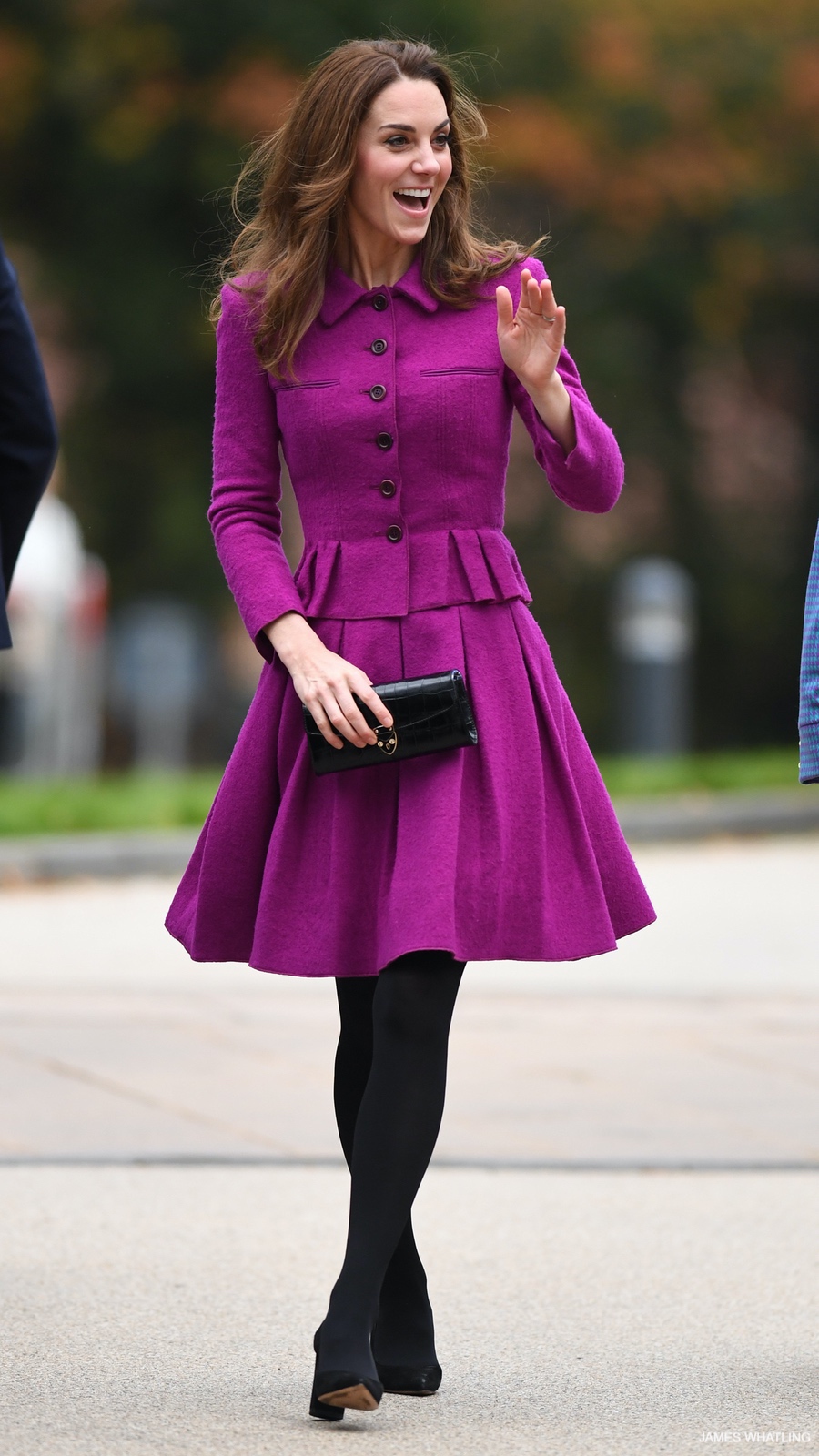 A smiling, happy Kate Middleton waving, wearing a vibrant magenta skirt suit and black tights.