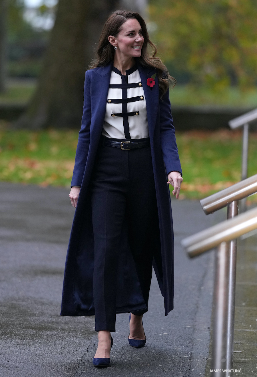 In this navy blue look, Kate radiates elegance and poise. She wears a navy blue and white military blouse trucked into navy trousers, with a long coat on top.