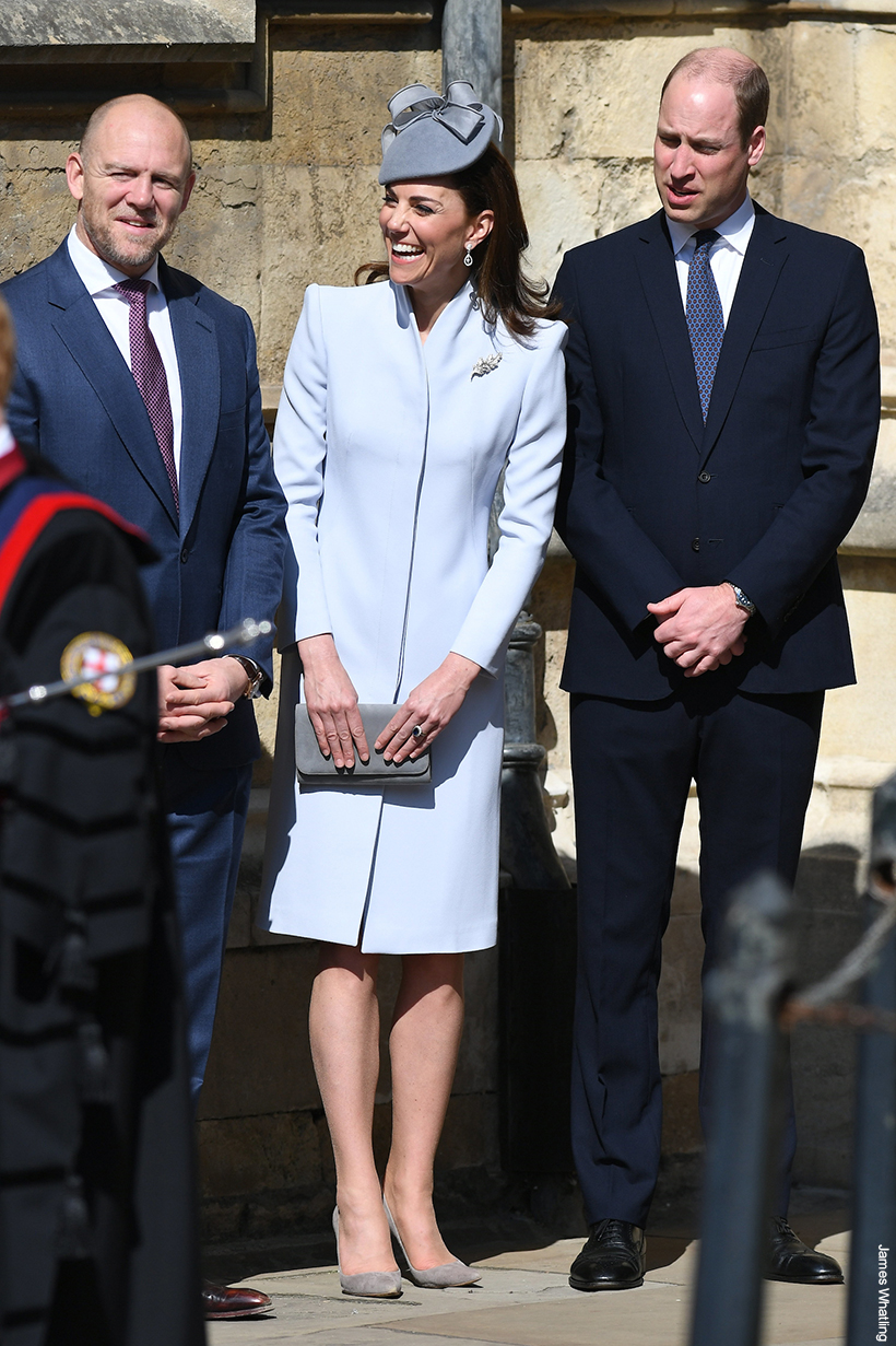 Kate Middleton rewearing her dove grey Alexander McQueen coat with updated accessories at Easter service in Windsor, 2019. The Princess is flanked by Mike Tindall and her husband William. She is laughing.