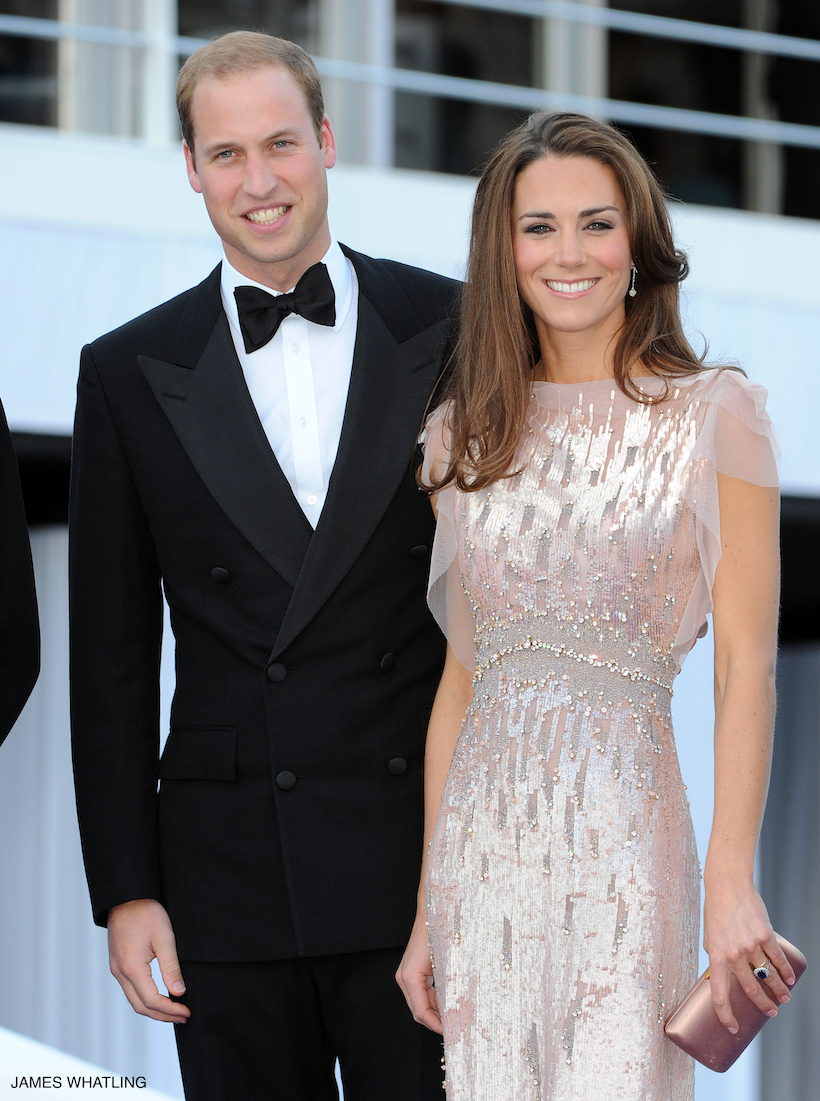 Kate Middleton stands smiling with Prince William as the pair pose for a photo at the 2011 Ark Gala. The Princess faces the camera wearing the iconic pink dress by Jenny Packham.