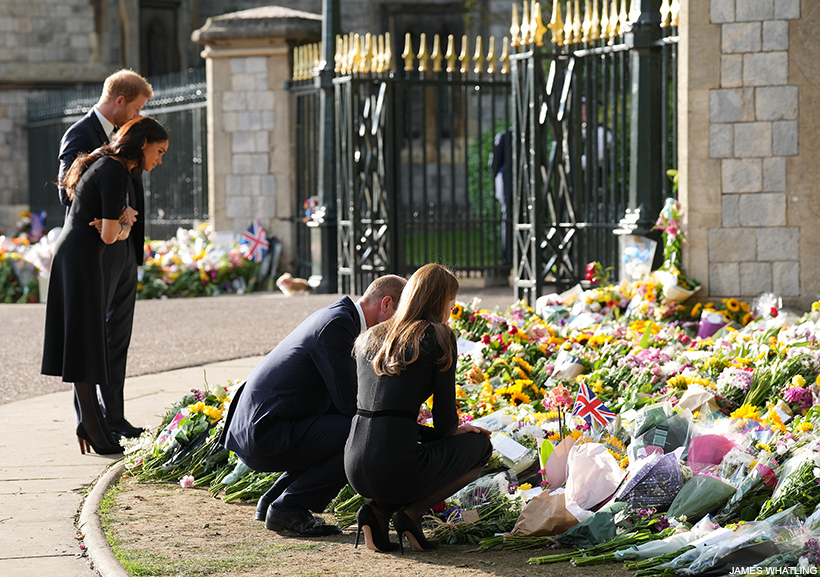 Harry and Meghan standing to look at floral tributes to the Queen outside of Windsor Castle.  Kate and William crouch nearby. 