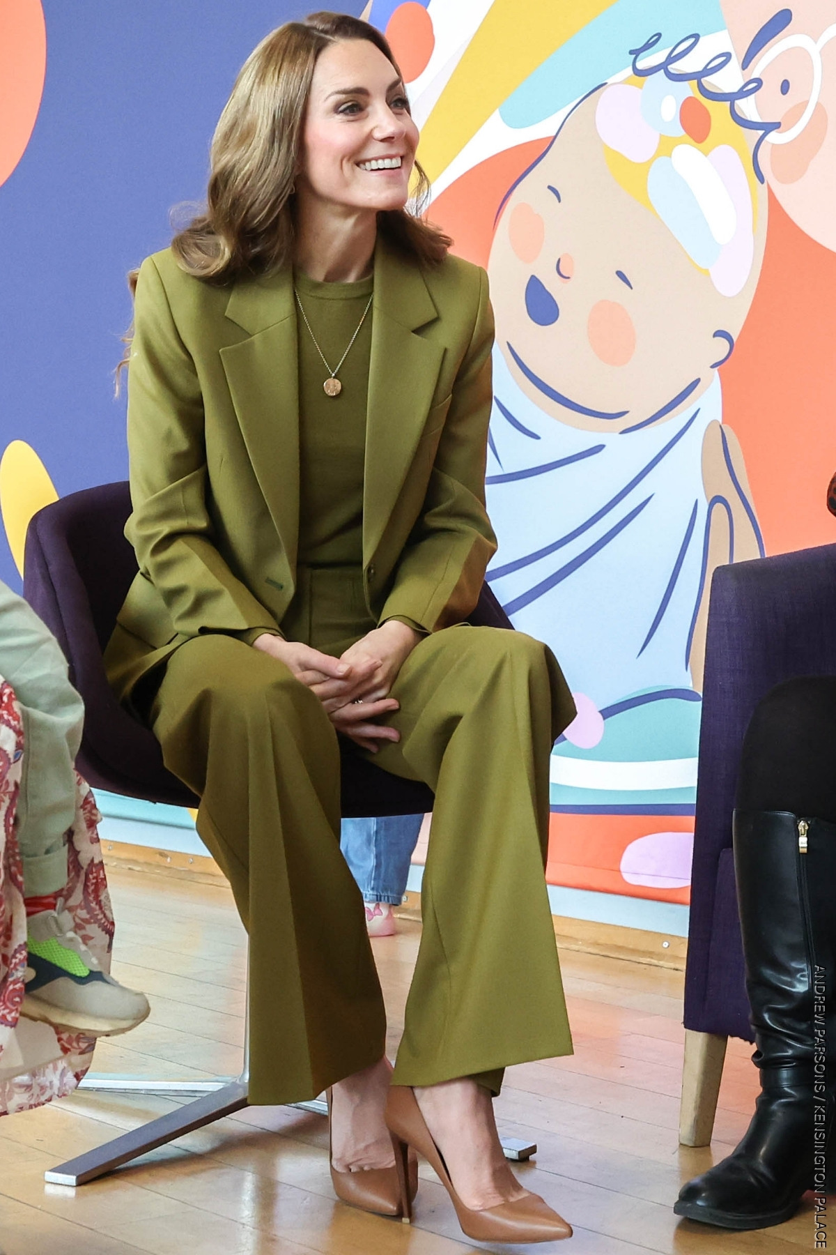 Princess of Wales, seated, wearing an olive green suit with matching olive green sweater. She finishes the look with a pair of golden brown heels by Ralph Lauren.