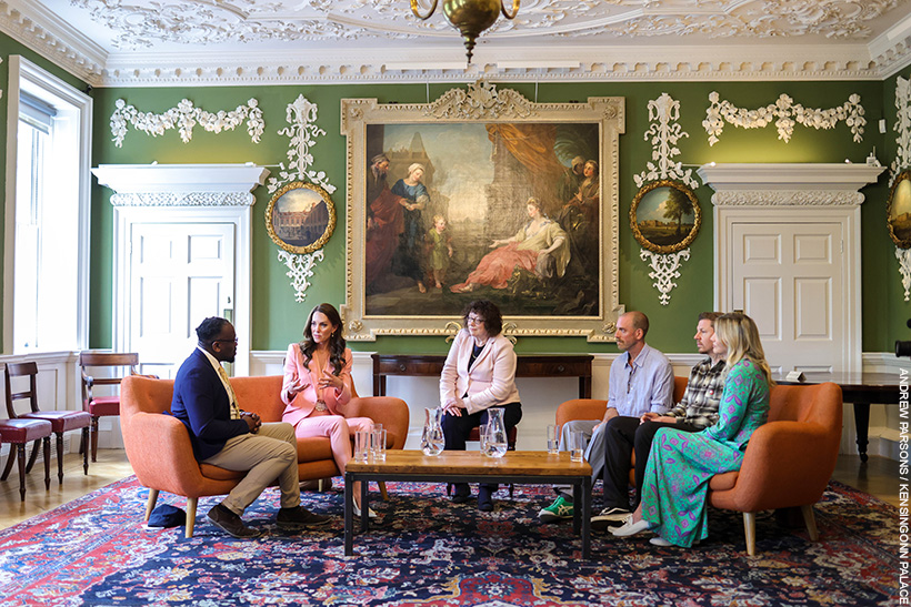 Kate Middleton chatting with people inside the Foundling Museum. She's wearing a pink suit with pearl accessories.