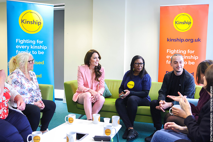 Kate Middleton chatting with people at a Kinship support group. She's wearing a pink suit with pearl accessories.