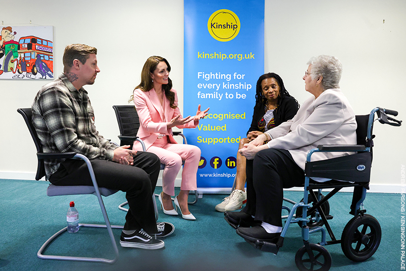 Kate Middleton chatting with people at a Kinship support group. She's wearing a pink suit with pearl accessories.