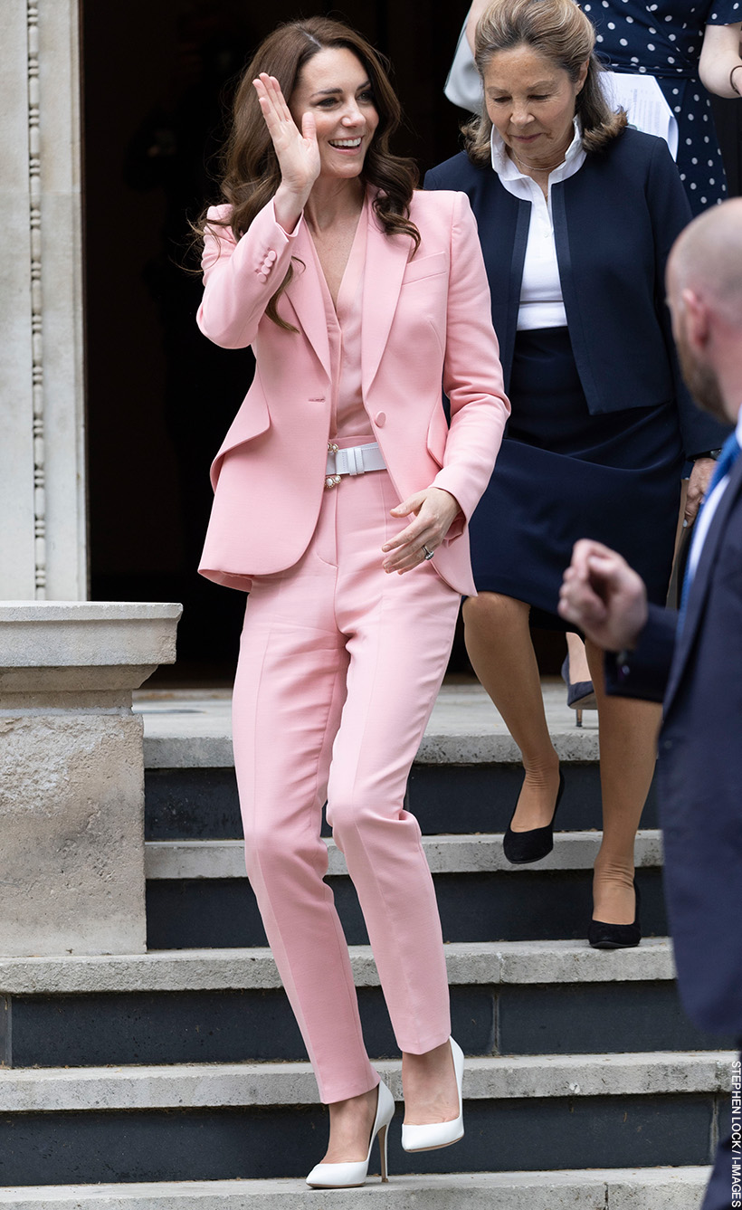 Kate Middleton waving as she leaves the Foundling Museum. She's wearing a pink suit with pearl accessories and white heels.