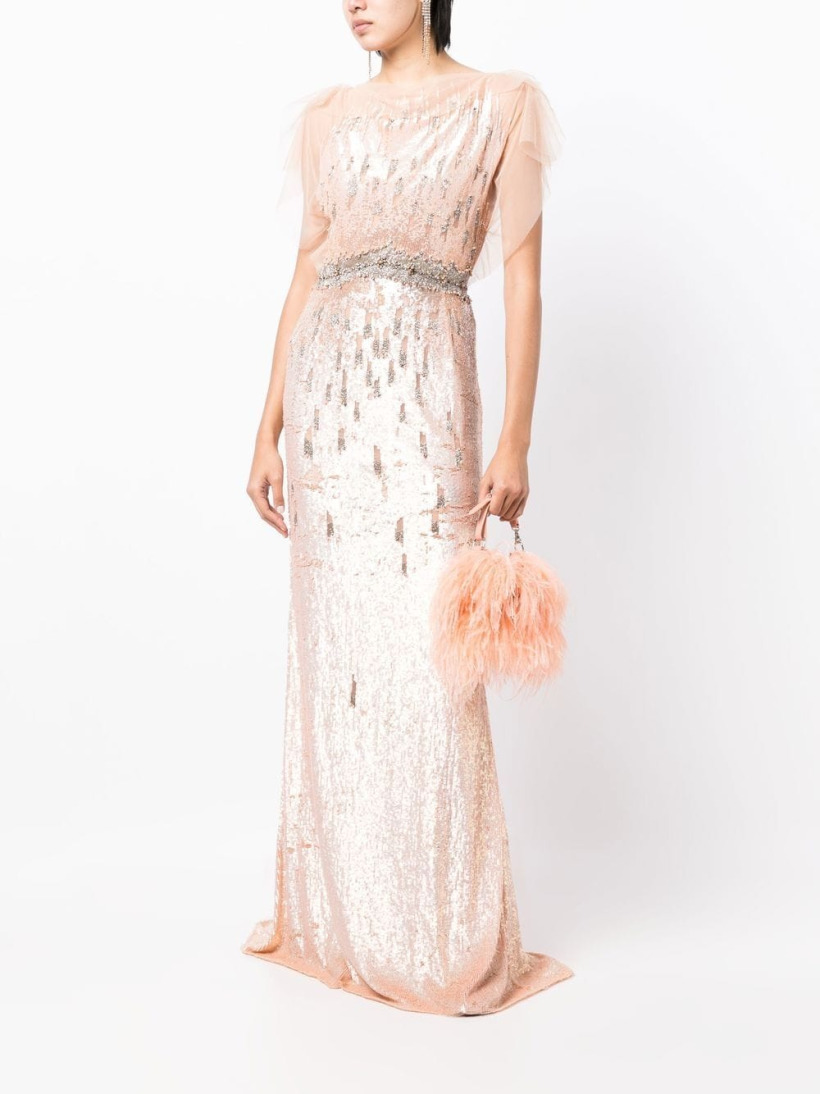 A shot of a model wearing the pink sequinned dress, while holding a fluffy pink handbag. The model stands in front of a white background.