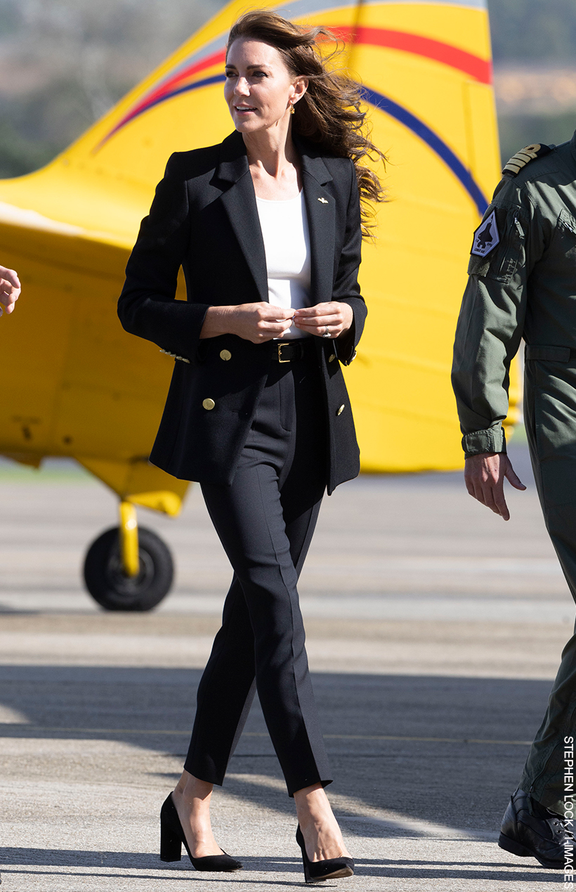Kate Middleton visited RNAS Yeovilton wearing a black blazer, white t-shirt and black trousers. She's walking with naval officers in front of a bright yellow plane, which contrasts with her black outfit.