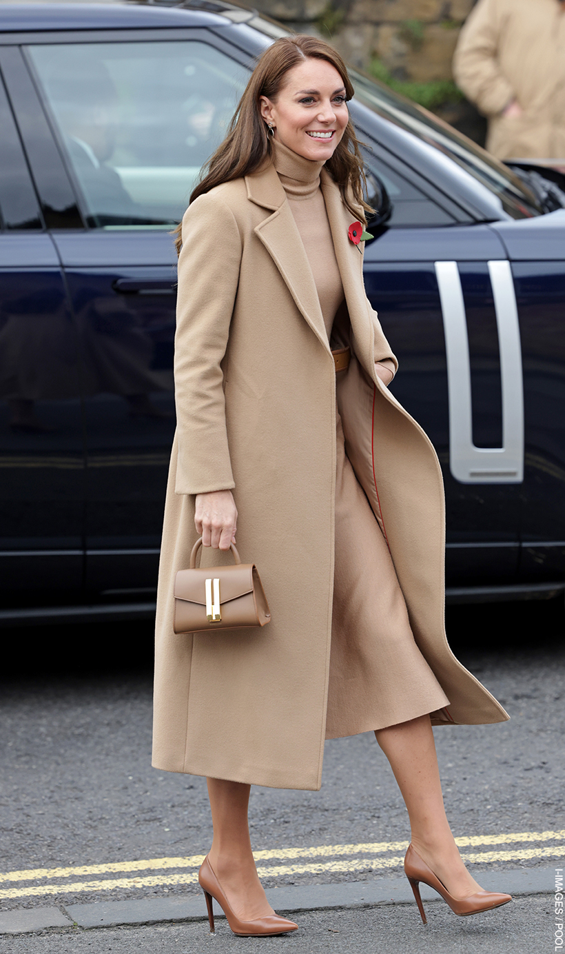 Kate Middleton, wearing a coat, skirt and top in matching camel tones, carrying the toffee coloured Demellier Nano Montreal bag. She is walking away from a car.