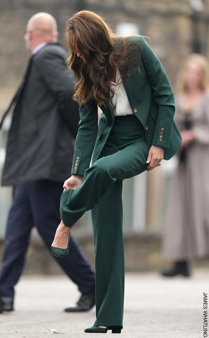 Kate Middleton lifting her leg up and pulling the hem of her green suit out of her Emmy London Josie pumps. You can clearly see the block heeled shoe in the image.
