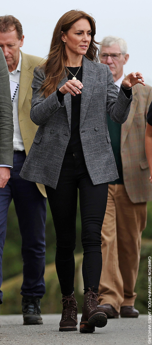 The Princess of Wales in Cornwall. The Princess wears a grey check blazer, black sweater, gold necklace, gold earrings, black jeans and brown combat boots.