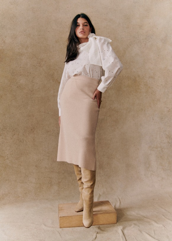 Product image from Sézane showing the model wearing the cream knit skirt. A white Broderie Anglaise blouse is tucked in the top of the skirt.