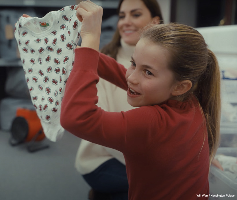 Charlotte shows somebody off camera the babygro printed with welsh dragons