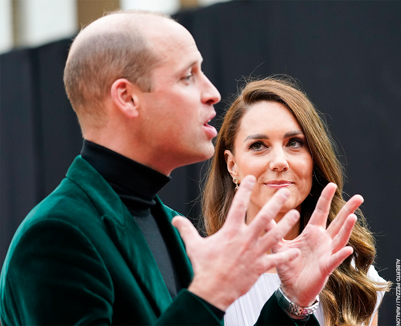 William, stood in a green jacket, is passionately expressing something to a person out of shot. Kate looks on, smiling, with a look of pride in her eyes.