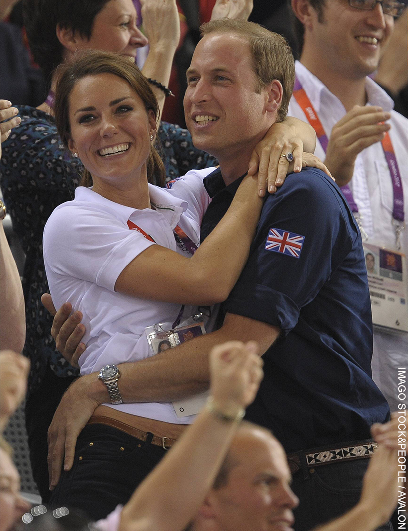 Prince William and Kate Middleton embracing. Dressed in sporty polo shirts, the pair hug in celebration. Both smiling, Kate grabs William’s shoulders and he has his hands around her waist.