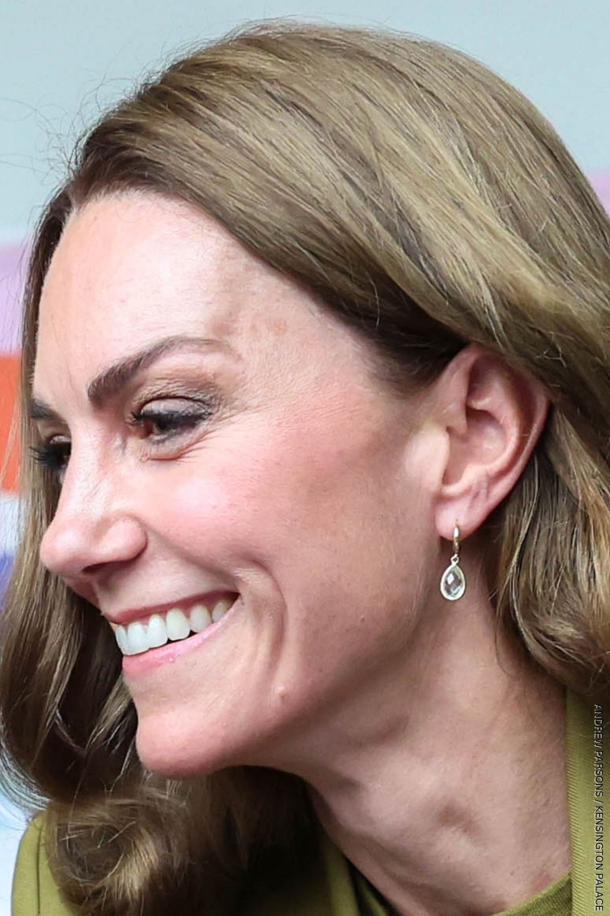 A really tight shot of the Princess of Wales looking to the side and smiling, she is wearing a pair of green amethyst pear drop earrings.