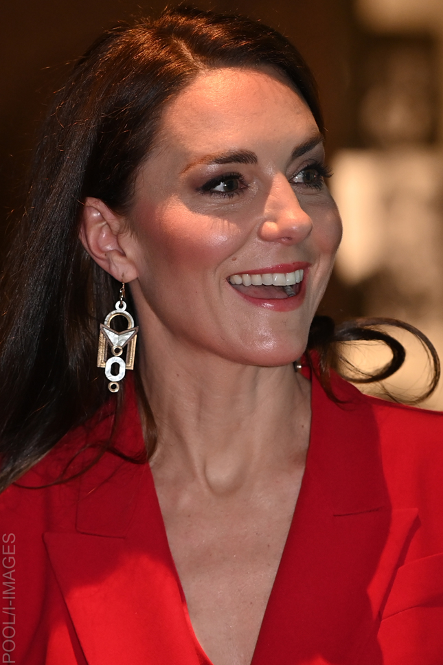 Kate Middleton smiling in her bold red suit, showing the plunging neckline and statement earrings at the Shaping Us launch.
