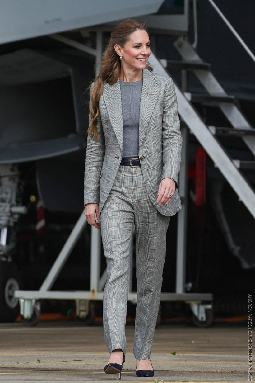 The Princess of Wales walking and smiling wearing a grey checked suit. Underneath the blazer, she is wearing a grey fine knit sweater by Alexander McQueen.