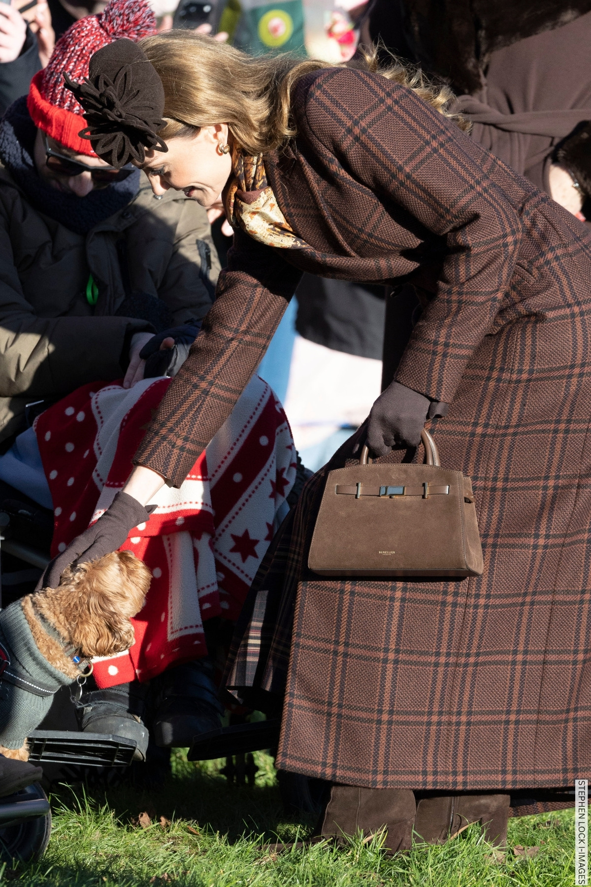 The Princess of Wales carrying the bag on Christmas Day, petting a dog. She carries her brown suede handbag.