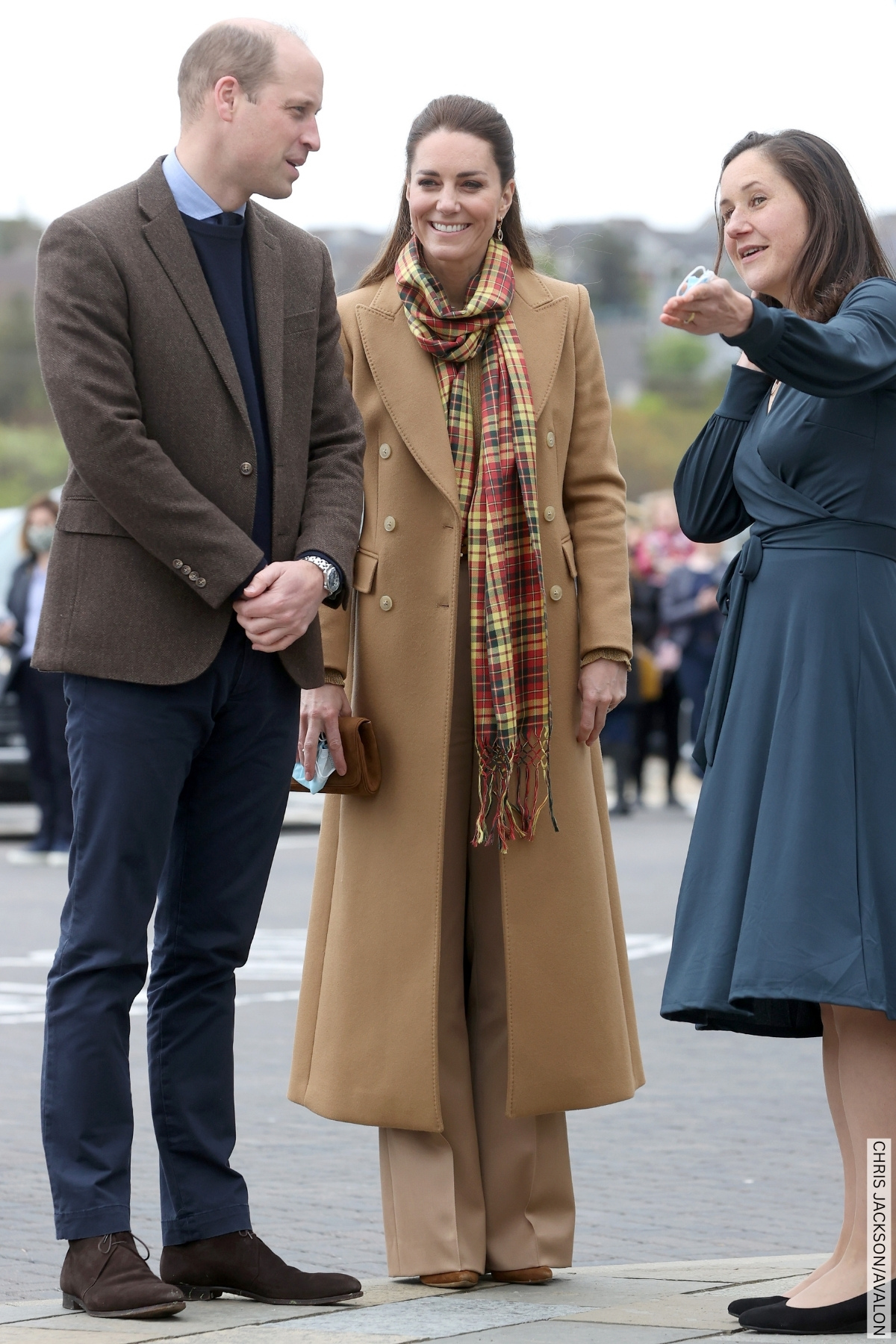 The Princess and Prince of Wales chatting with a lady.  The Princess wears a long tartan scarf over her camel brown coat. 