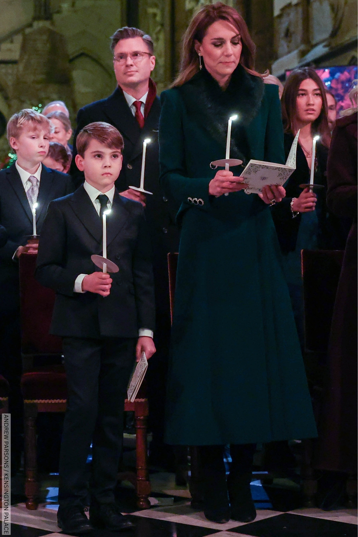 The Princess of Wales, dressed in her green fur topped coat, at the Christmas Carol service. She is stood with her son Lewis, both holding lit candles.